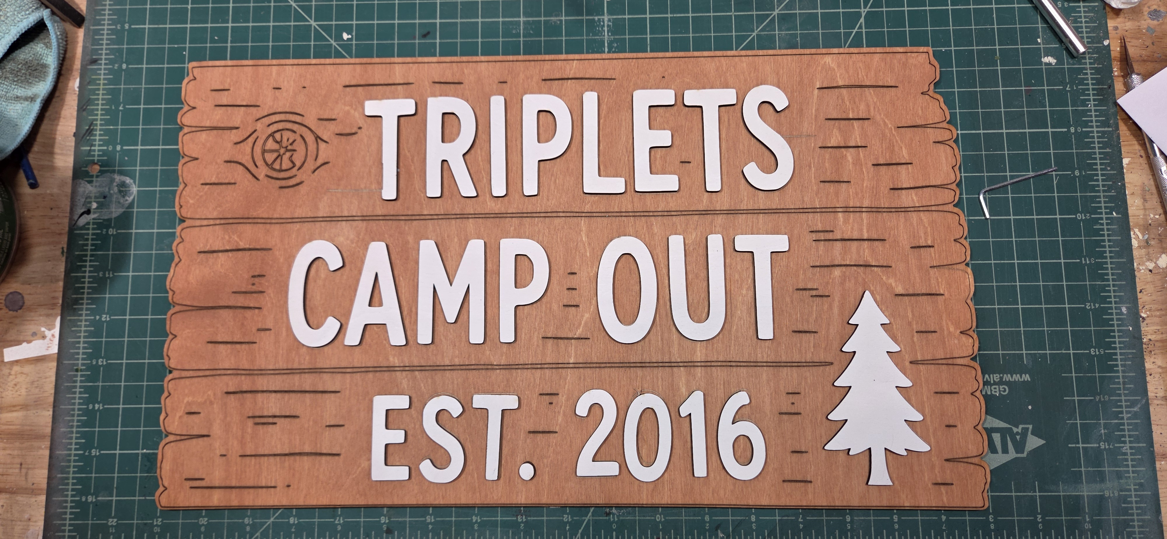 Completed coordinated wooden camp sign set, upright on the workshop table